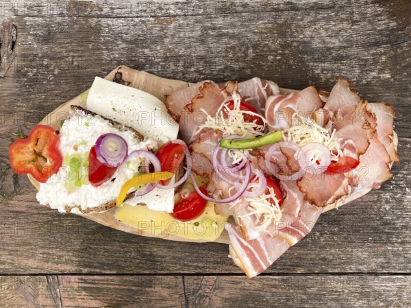 Typical snack on the alpine pasture, bacon bread and cheese bread on wooden plate on wooden table,