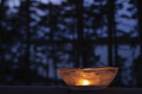 Ice bowl illuminated by burning tea light stands on balcony balustrade, forest at the onset of