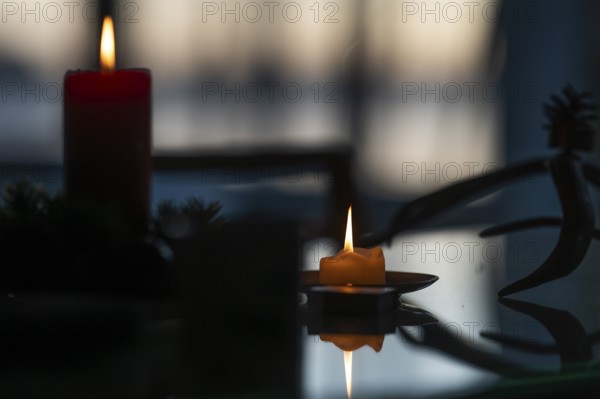 Two candles stand on a table in front of a window at dusk and create a Christmas atmosphere,