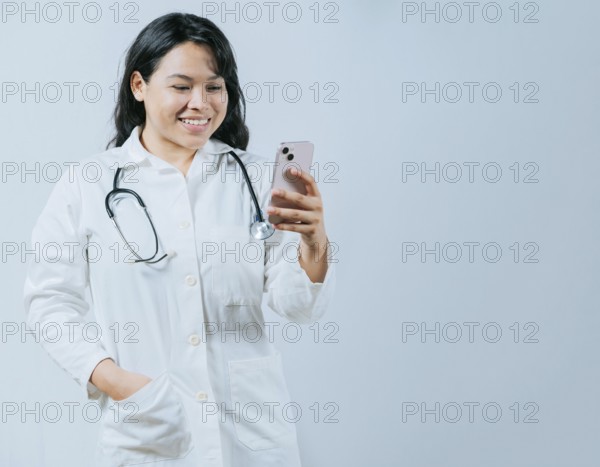 Female healthcare worker holding cellphone. Smiling asian doctor using smartphone isolated, Young