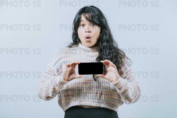 Surprised asian woman showing phone screen isolated. Beautiful asian girl showing promotion on