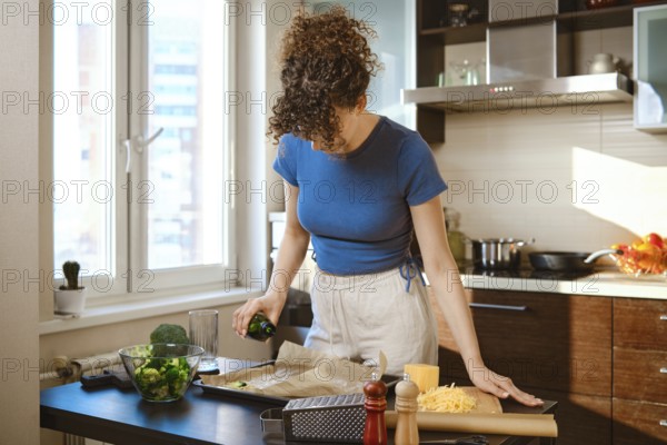 Woman pouring olive oil over the parchment. Ingredients are spread out on a counter near cooking