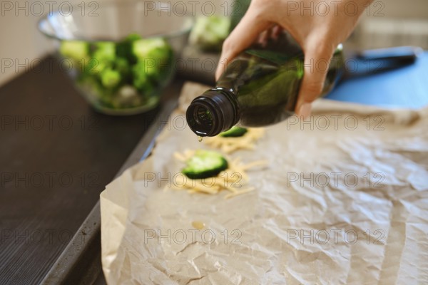 Broccoli florets and cheese are being prepared in a kitchen. Olive oil is drizzled on parchment to