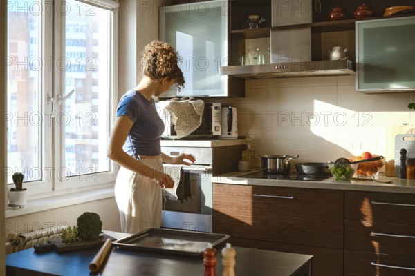 Woman turns on oven to preheat. The sunlight comes through the window. Various ingredients are on
