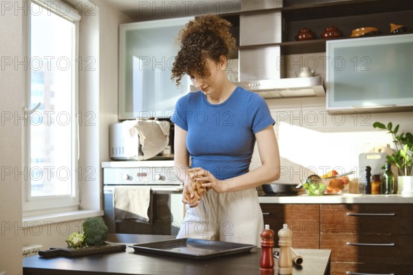 A woman crumples parchment to carefully lay it out on a baking sheet. She stands at a table,