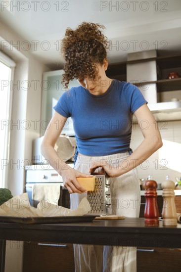 Woman grates cheese in a bright kitchen while preparing smashed broccoli. The scene shows cooking