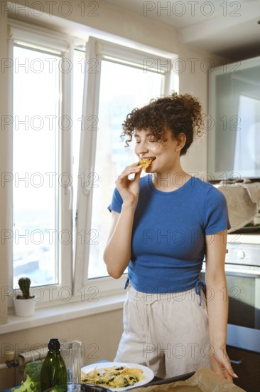 Woman bites smashed broccoli with cheese. The window opens to a city view. Fresh ingredients are on