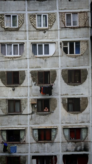 Dilapidated residential building with open windows and people in a simple environment, Tbilisi,