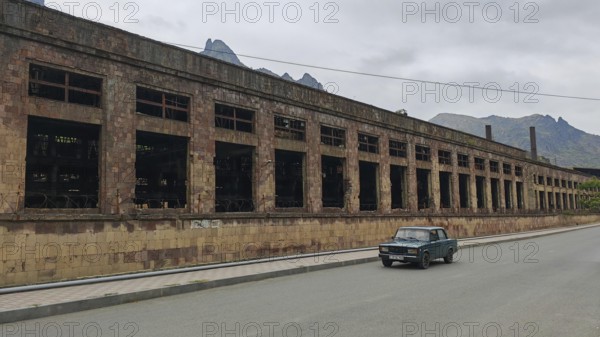 Abandoned large building and a car on a quiet road in the background mountains and clouds,