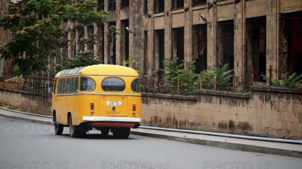 Old yellow bus runs on empty city street next to a weathered building, Alaverdi, Armenia