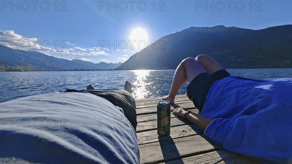 Two people relax on a jetty in front of an impressive mountain backdrop at the lake, Plav Lake,