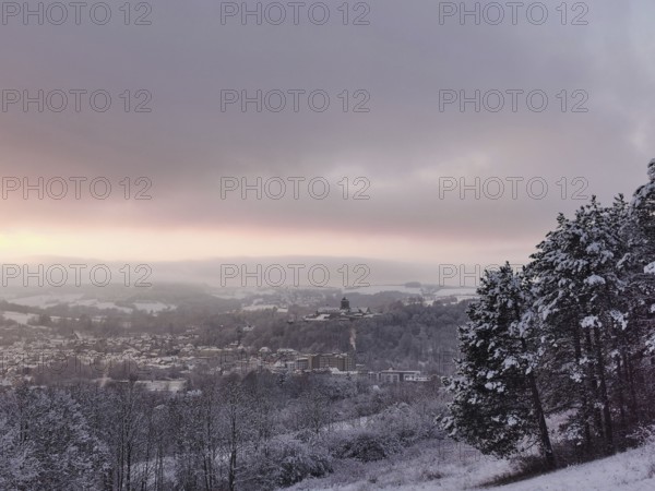 Snowy hills with a view of a village at sunset, view of Rosenberg Fortress and the town of Kronach,