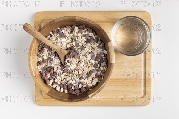 Rustic bowl with cereal and wooden spoon on a wooden board, water glass next door