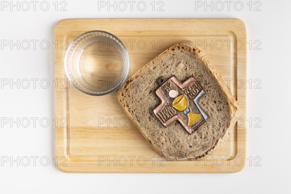 Bread with cross symbol on a wooden board with a glass of water next to it, white background