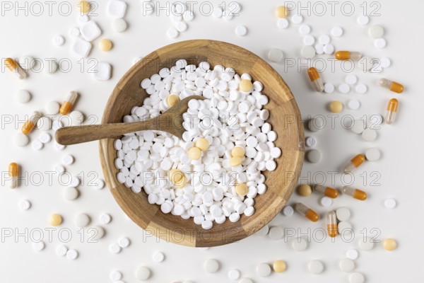 Wooden bowl filled and surrounded by tablets and capsules on light background