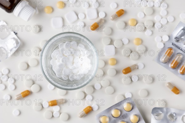 Scattered white tablets and a glass of water on a table