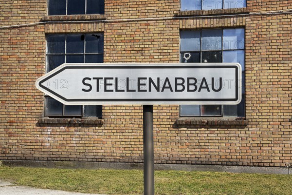 (photo montage) Directional arrows with the inscription JOB REDUCTION in front of an old industrial