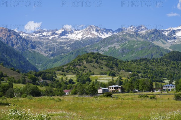 Picturesque mountain landscape with snowy peaks, green hills and meadows under blue skies,