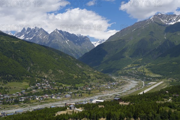 A view of a valley with a river surrounded by mountains and a village in the foreground, right