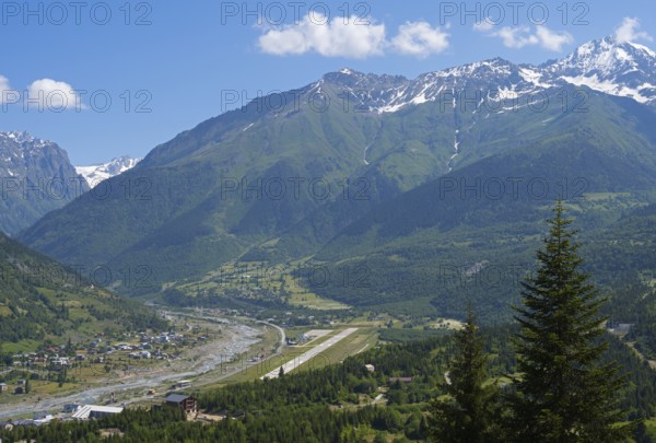 Valley with river and adjacent mountains under a bright blue sky, in the middle an airport, Mestia,
