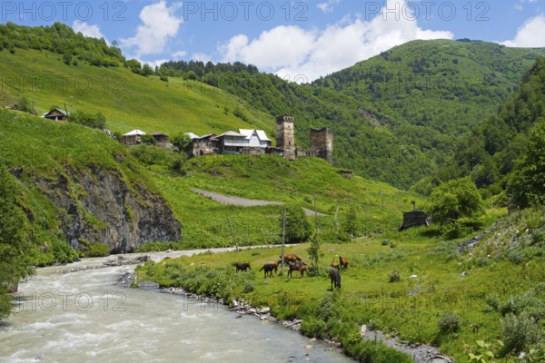 River surrounded by green countryside and hills with a village in the background, horses on the