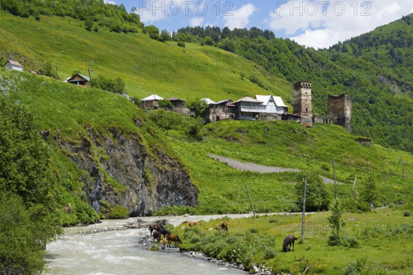 Idyllic landscape with river and village on a hill, horses grazing in the foreground, Davberi on