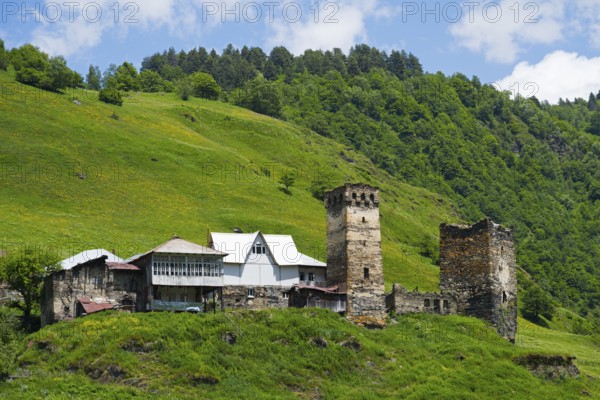 Medieval village with tower on a hill in the background, surrounded by green landscape and clear
