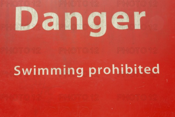 Danger Swimming Prohibited in white letters on red painted metal public notice sign in public park,