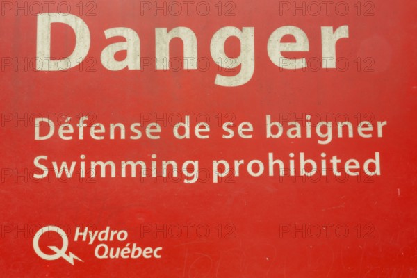 Bilingual French and English Danger Swimming Prohibited in white letters on red painted metal