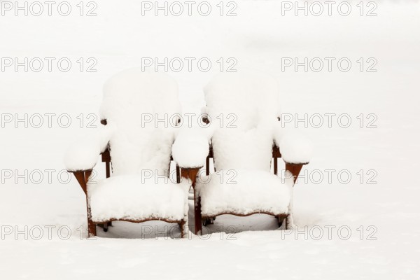 Two brown stained wooden Adirondack chairs covered in freshly fallen winter like snow in public