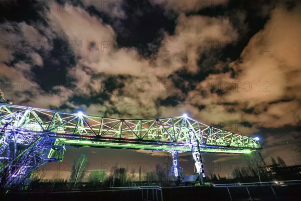 Illuminated bridge at night under a dramatically cloudy sky with green light, Landschaftspark