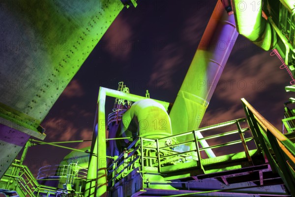 Detailed view of a metallic industrial plant illuminated with green and purple lights,