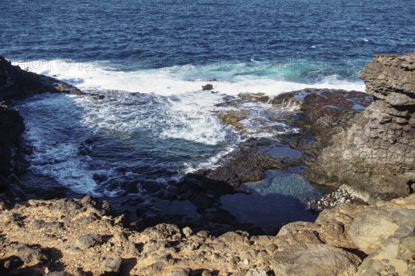 Coastal landscape with rocks in the foreground and riverbank surf in the background, Playa Blanca