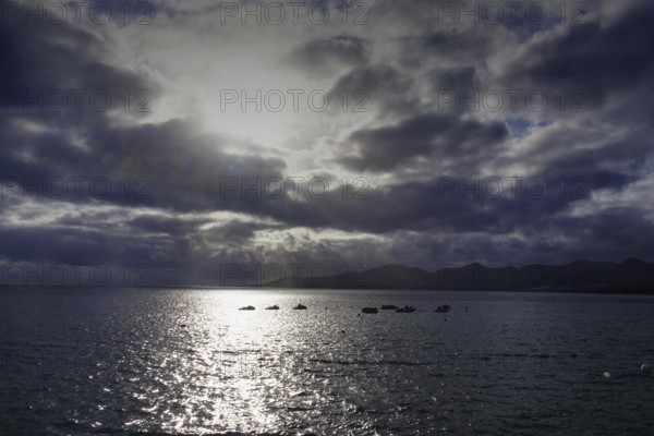 Dramatic atmosphere over the sea, clouds obscuring the sun, reflecting light on the water, Puerto