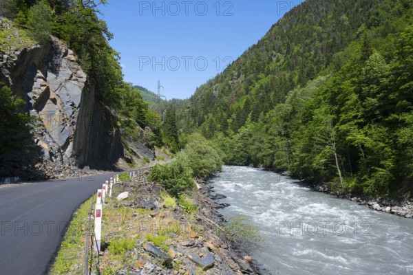 Mountain road next to a flowing river in a green, wooded landscape in clear summer weather, Enguri
