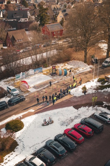 Aerial view of a street scene with people and cable drums in the snow, fiberglass groundbreaking,