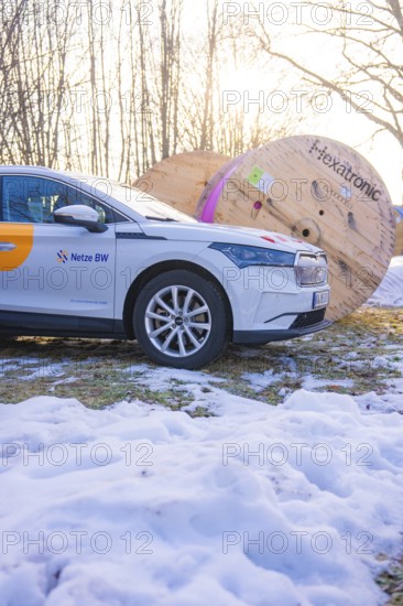 A car stands next to large rolls of cable on a snow-covered meadow in winter, fibreglass