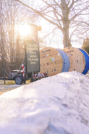 Cable rolls and a construction site sign along a snowy road when the sun is low, fibreglass