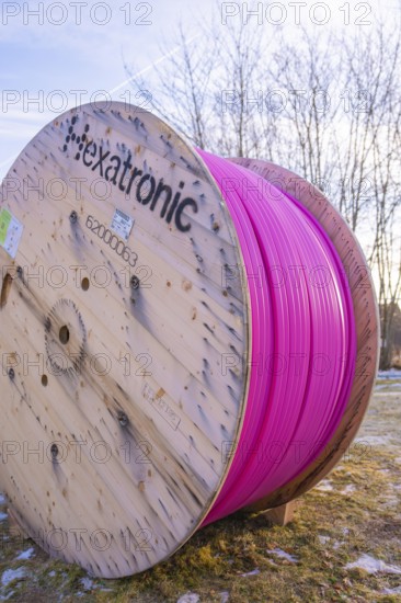 A large pink cable reel stands in a meadow under a blue sky in winter, fiberglass groundbreaking,