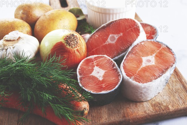 Potatoes, salmon, garlic, onion, and herbs are placed on a wooden cutting board. These ingredients