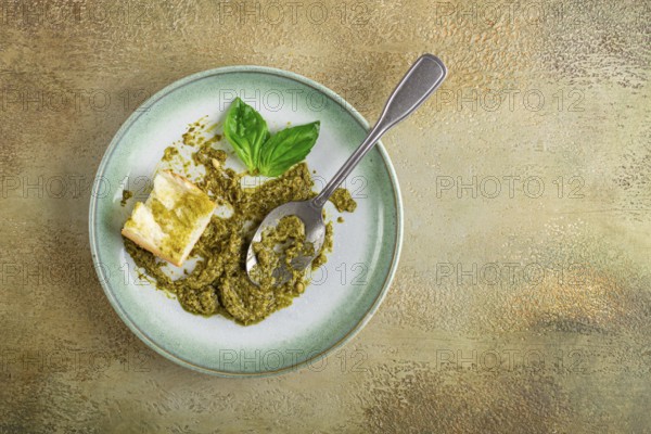 On a platter is a pesto sauce made from fresh basil, with a slice of bread and a spoon on a plate.