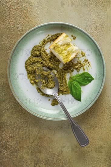 On a platter is a pesto sauce made from fresh basil, with a slice of bread and a spoon on a plate.