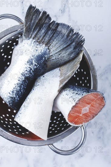 Fish tails are placed in a colander on a marble counter. The colander allows water to drain away