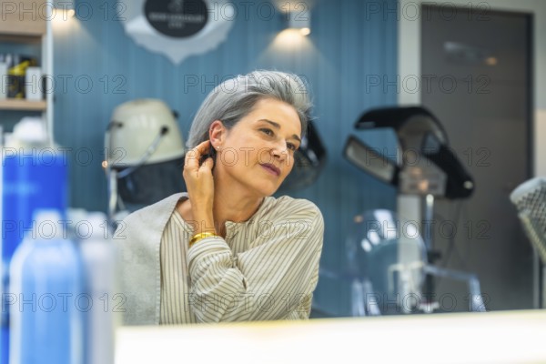 Senior woman with silver hair smiles, admiring her stylish short haircut in a salon mirror, feeling
