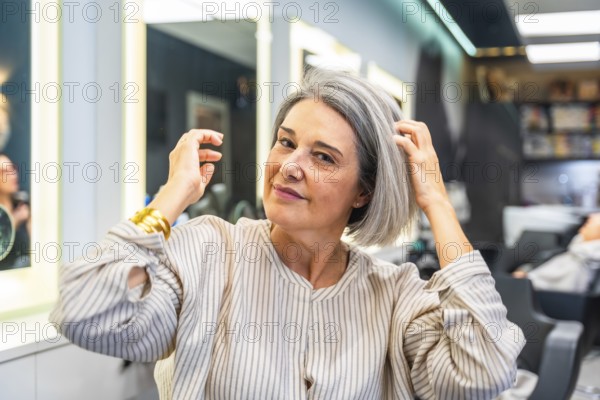 Senior woman smiling and touching her healthy gray hair, sitting in a modern hair salon, ready for