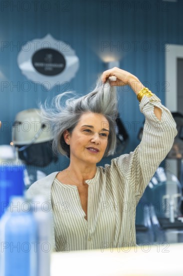 Mature woman looking at her reflection and touching her natural gray hair after a recent blow dry