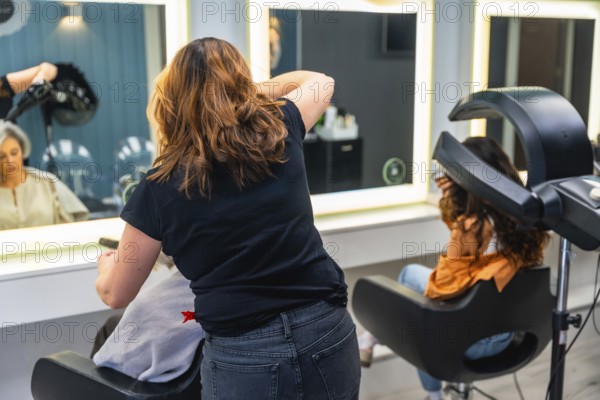 Hairdresser working on a client's hair in a professional beauty salon, with another client