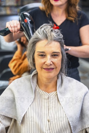 Mature woman sitting in a hair salon during a blow dry session, smiling confidently while a