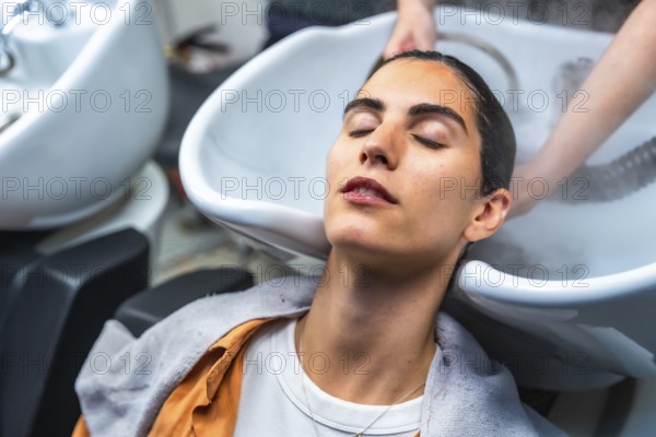 Woman closing her eyes while relaxing and receiving a professional hair wash and steam treatment at