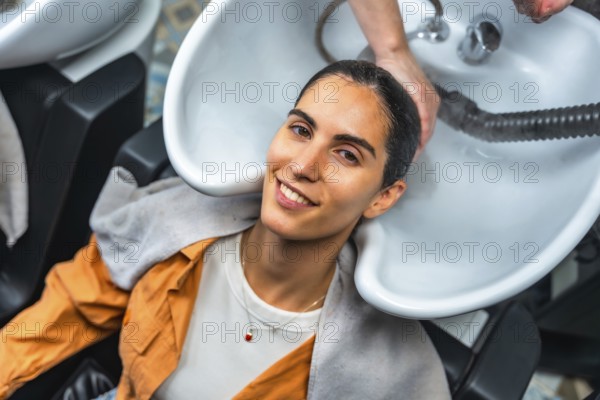 Young woman smiling and relaxing as a hairdresser shampoos and rinses her hair at a professional